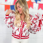Woman wearing a red and white letterman jacket with pom-poms in front of a colorful banner.
