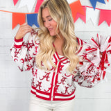 Woman wearing a red and white letterman jacket with pom-poms in front of a colorful banner.