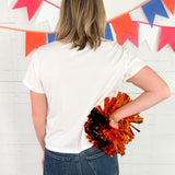 Person holding orange and black pom-poms in front of a colorful flag banner.