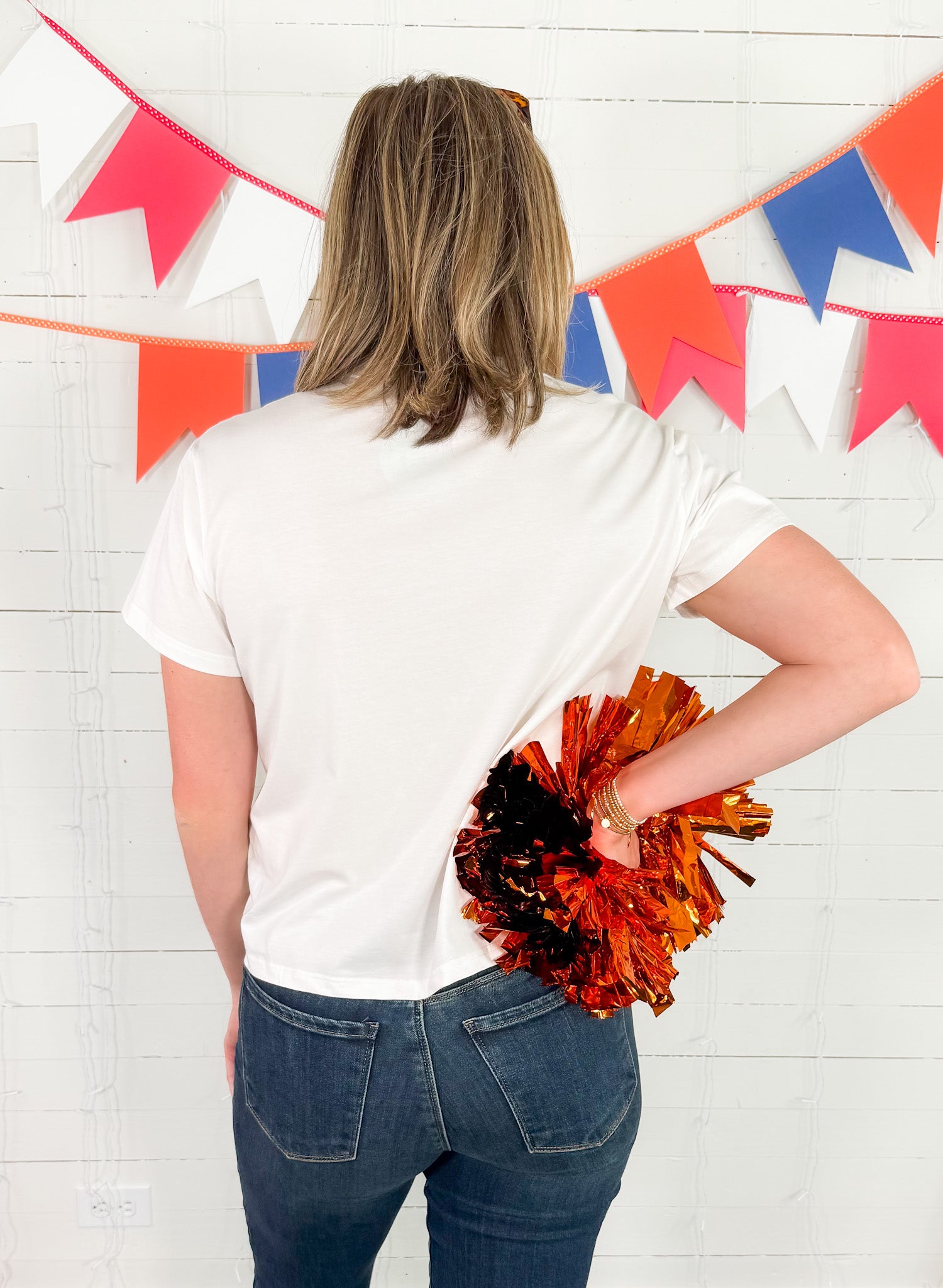 Person holding orange and black pom-poms in front of a colorful flag banner.