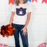 Person wearing a white t-shirt with a logo, holding pom-poms, standing in front of a colorful banner.
