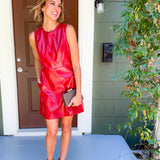 Woman in a red dress standing outside a house with a plant to the side.