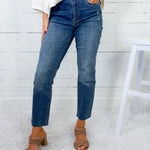 Person wearing blue jeans and brown sandals against a white wooden panel background