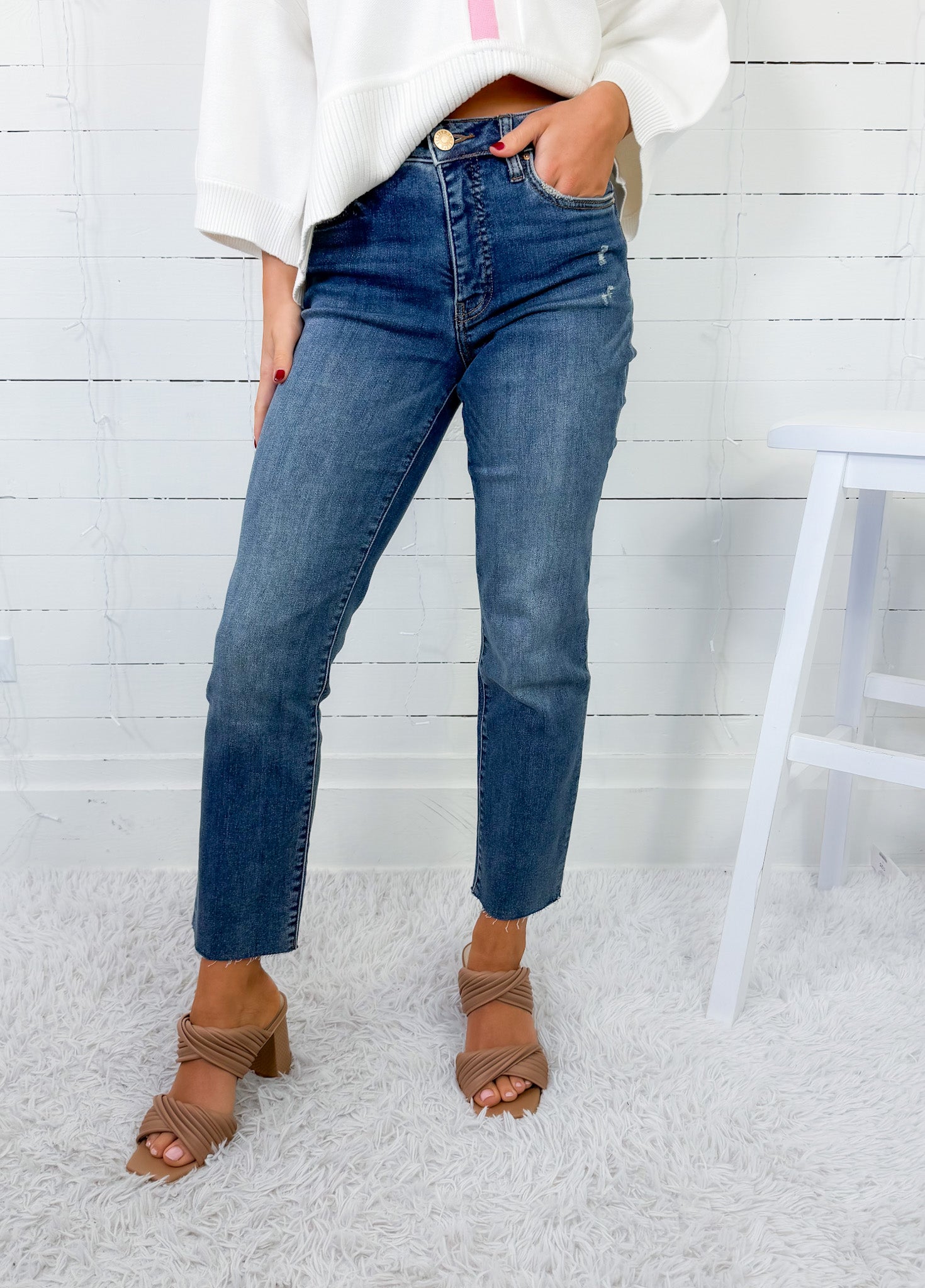 Person wearing blue jeans and brown sandals against a white wooden panel background