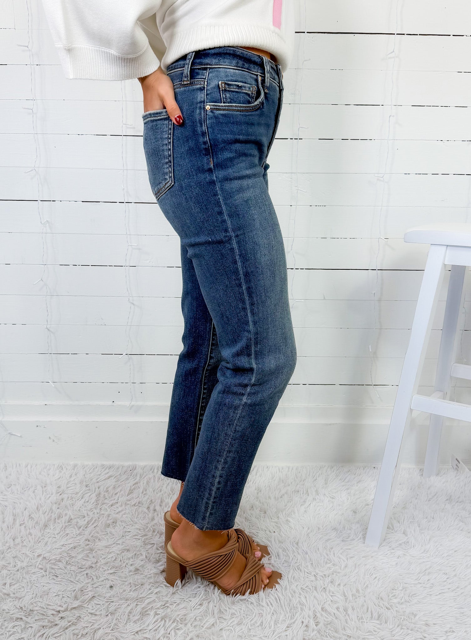 Person wearing blue jeans and a white sweater against a white wooden panel background