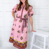 Woman wearing a pink patterned dress standing against a white wooden panel background