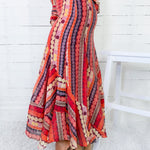 Colorful patterned dress worn by a person sitting on a white stool against a white wooden panel background.