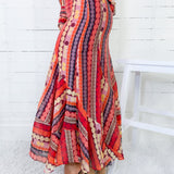 Colorful patterned dress worn by a person sitting on a white stool against a white wooden panel background.