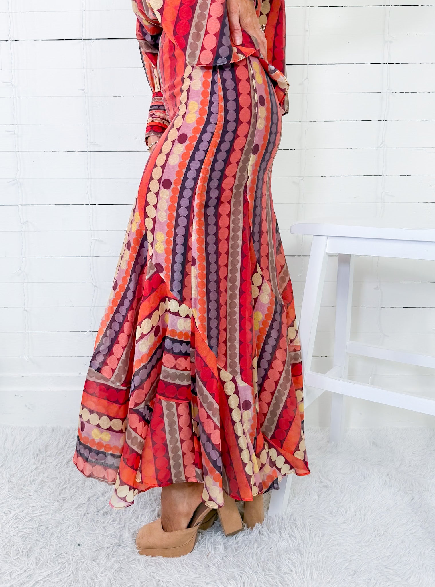 Colorful patterned dress worn by a person sitting on a white stool against a white wooden panel background.