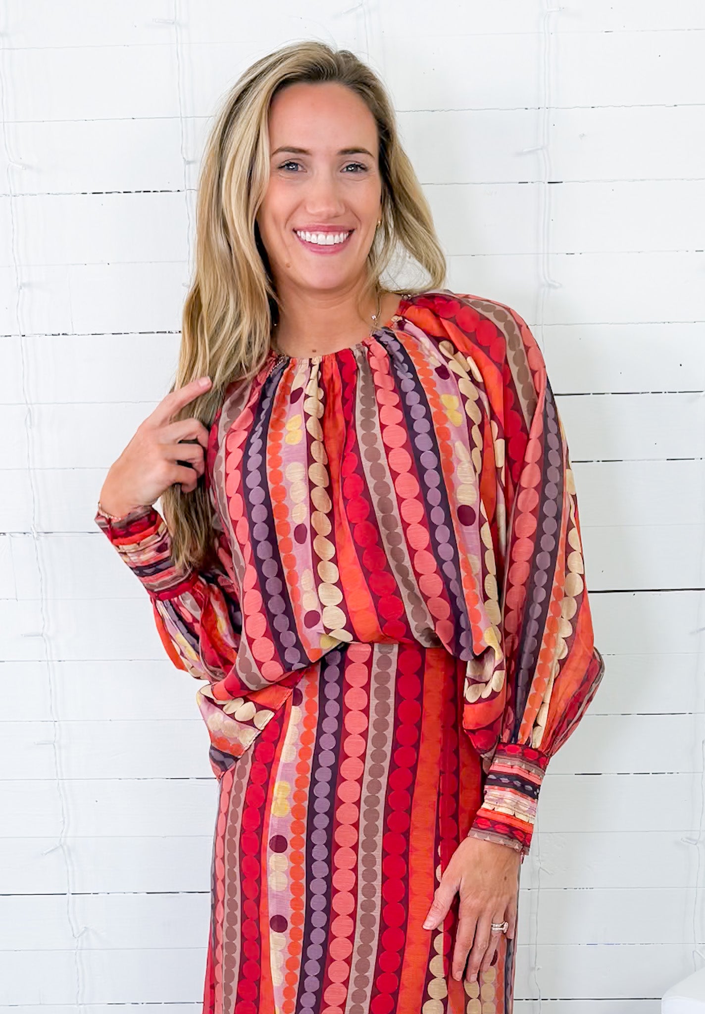 Woman wearing a colorful patterned dress against a white wooden background