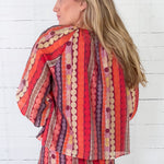 Woman wearing a colorful patterned outfit against a white wooden background