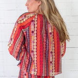 Woman wearing a colorful patterned outfit against a white wooden background