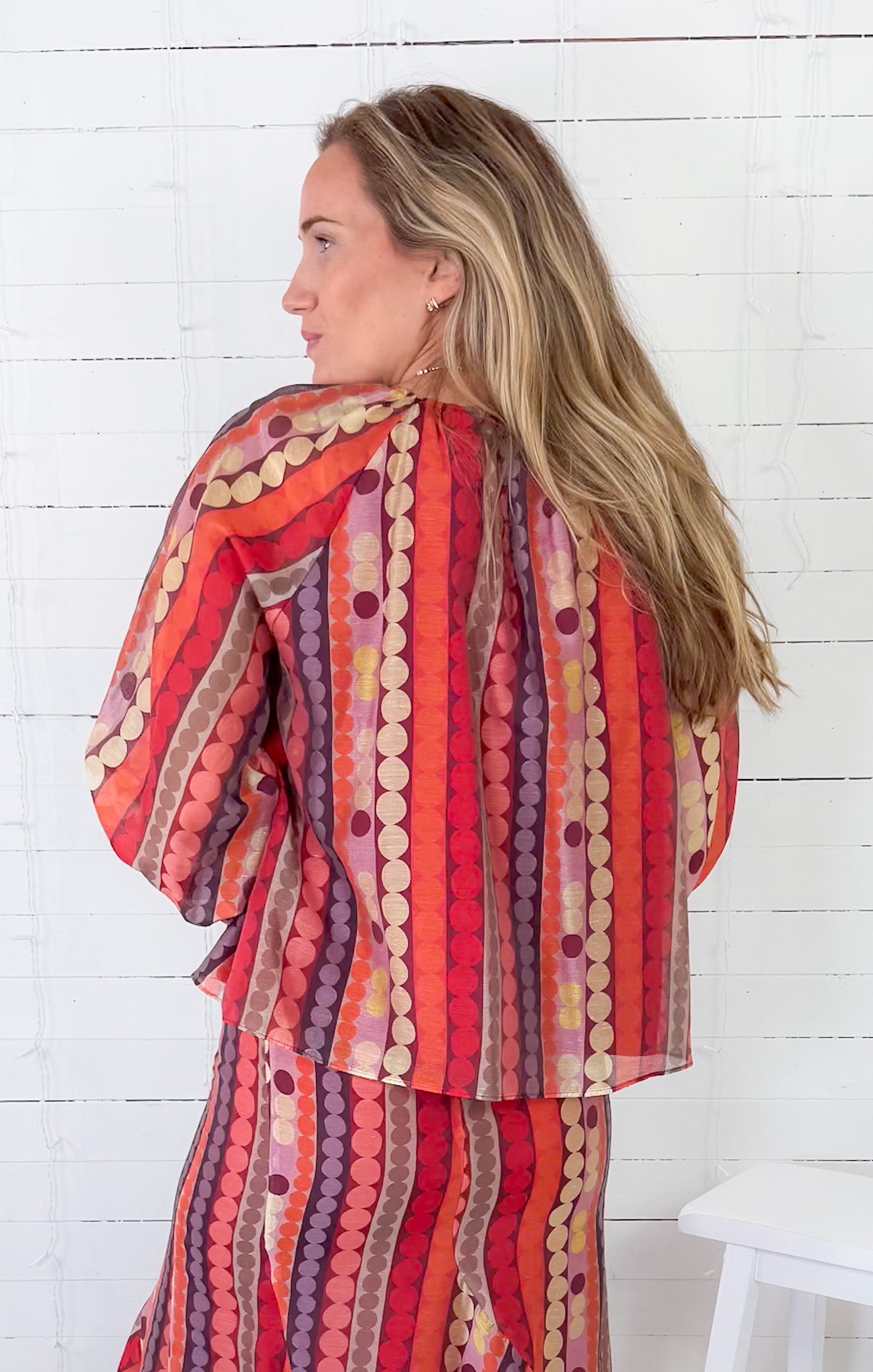 Woman wearing a colorful patterned outfit against a white wooden background