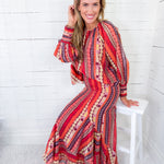 Woman wearing a colorful patterned dress sitting on a white stool against a white wooden panel background.