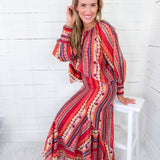 Woman wearing a colorful patterned dress sitting on a white stool against a white wooden panel background.