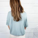 Person wearing a light blue sweater and white pants against a white wooden panel background