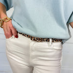 Light blue sweater, white pants, and leopard print belt against a white background