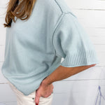 Light blue sweater worn by a person against a white wooden panel background
