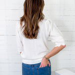 Person wearing a white sweater and blue jeans against a white wooden panel background