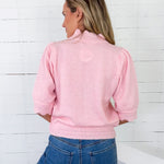 Woman wearing a pink jacket and blue jeans against a white wooden panel background