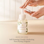 Hand holding a bottle of Thymes Frasier Fir hand soap with a neutral background