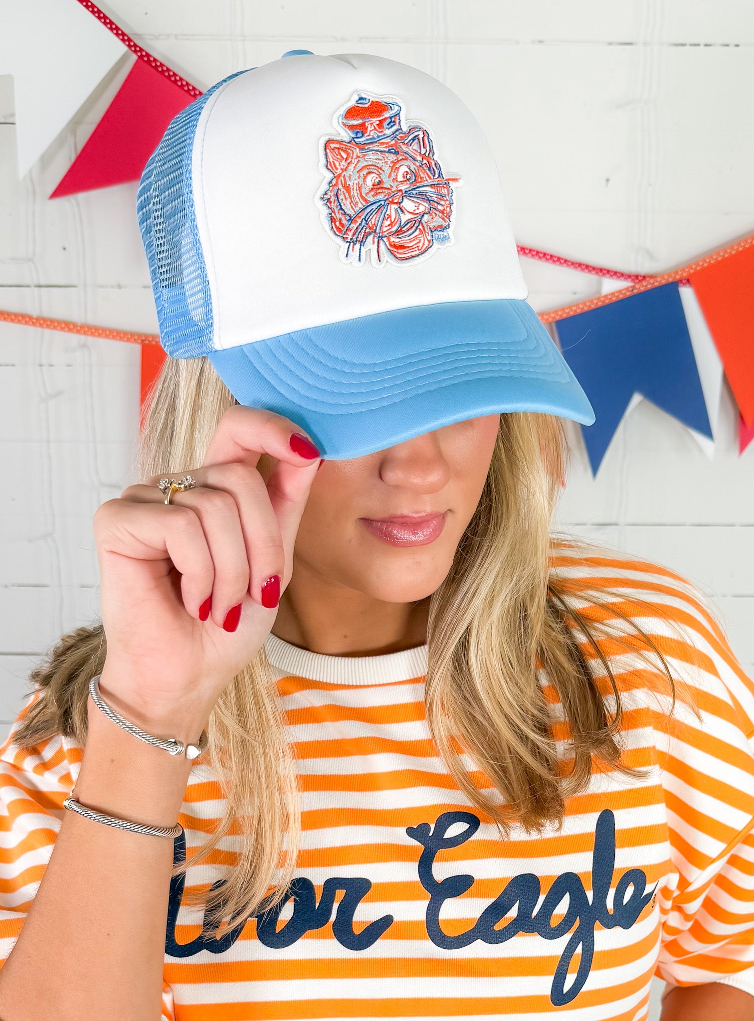 Person wearing a blue and white cap with a logo, holding it up to their face, against a colorful flag background.