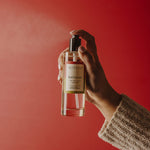 Hand holding a bottle of Votivo Red Currant body spray against a red background