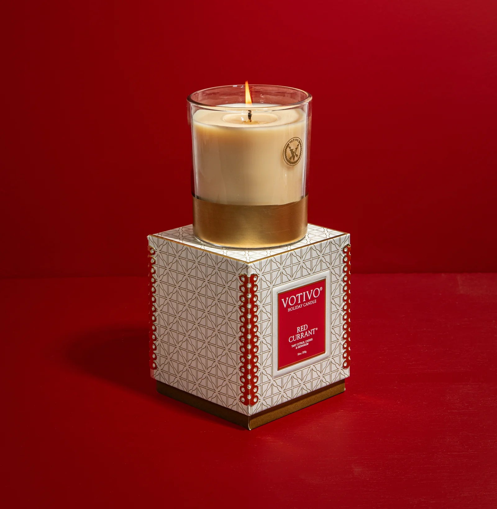 Votivo candle on its packaging against a red background