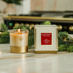 Votivo Red Currant candle and its packaging on a decorative surface with greenery.
