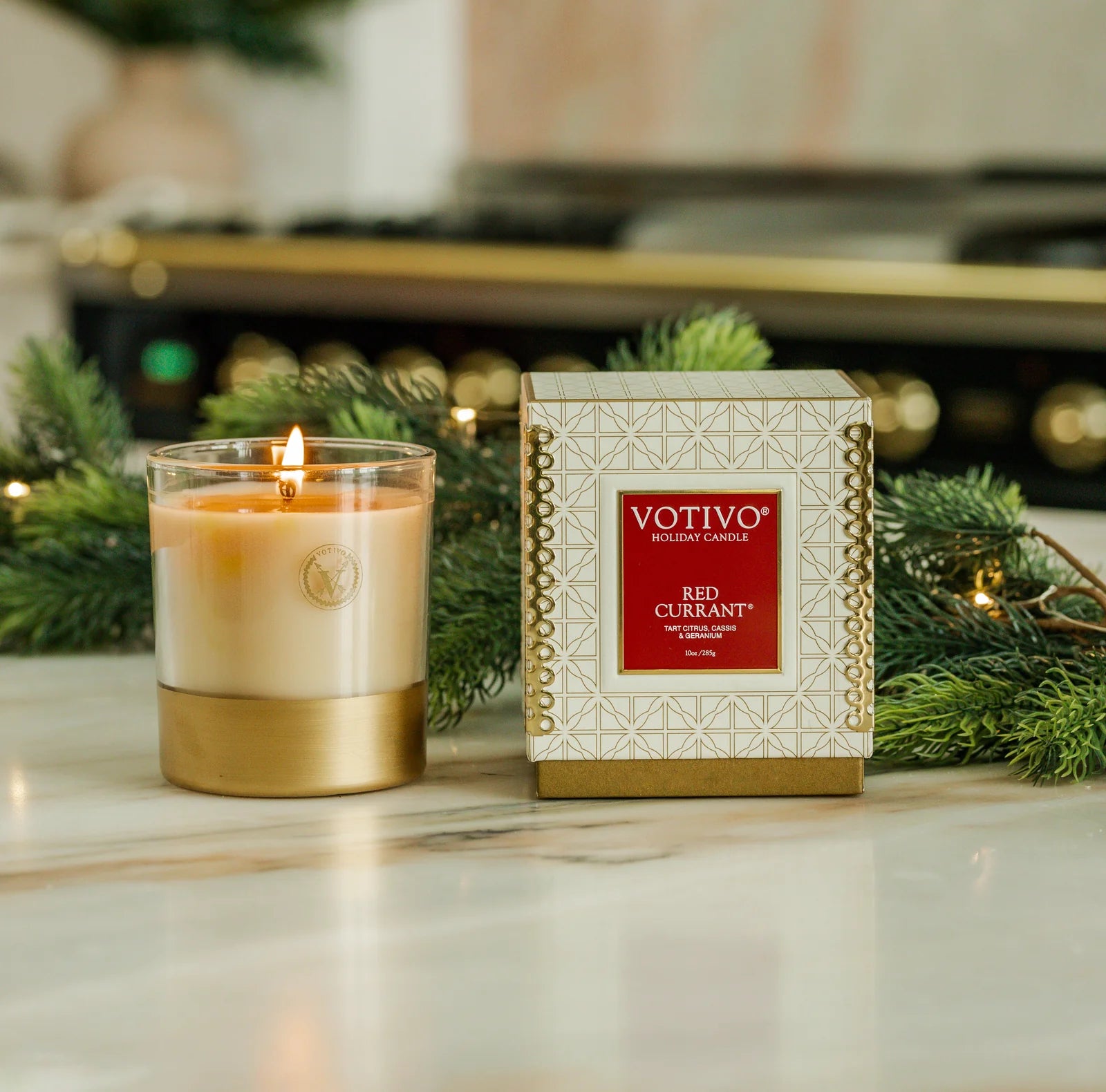 Votivo Red Currant candle and its packaging on a decorative surface with greenery.