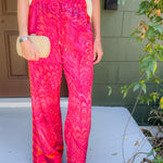 Person wearing bright pink patterned pants with a white top, standing on a porch.