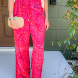 Person wearing bright pink patterned pants with a white top, standing on a porch.