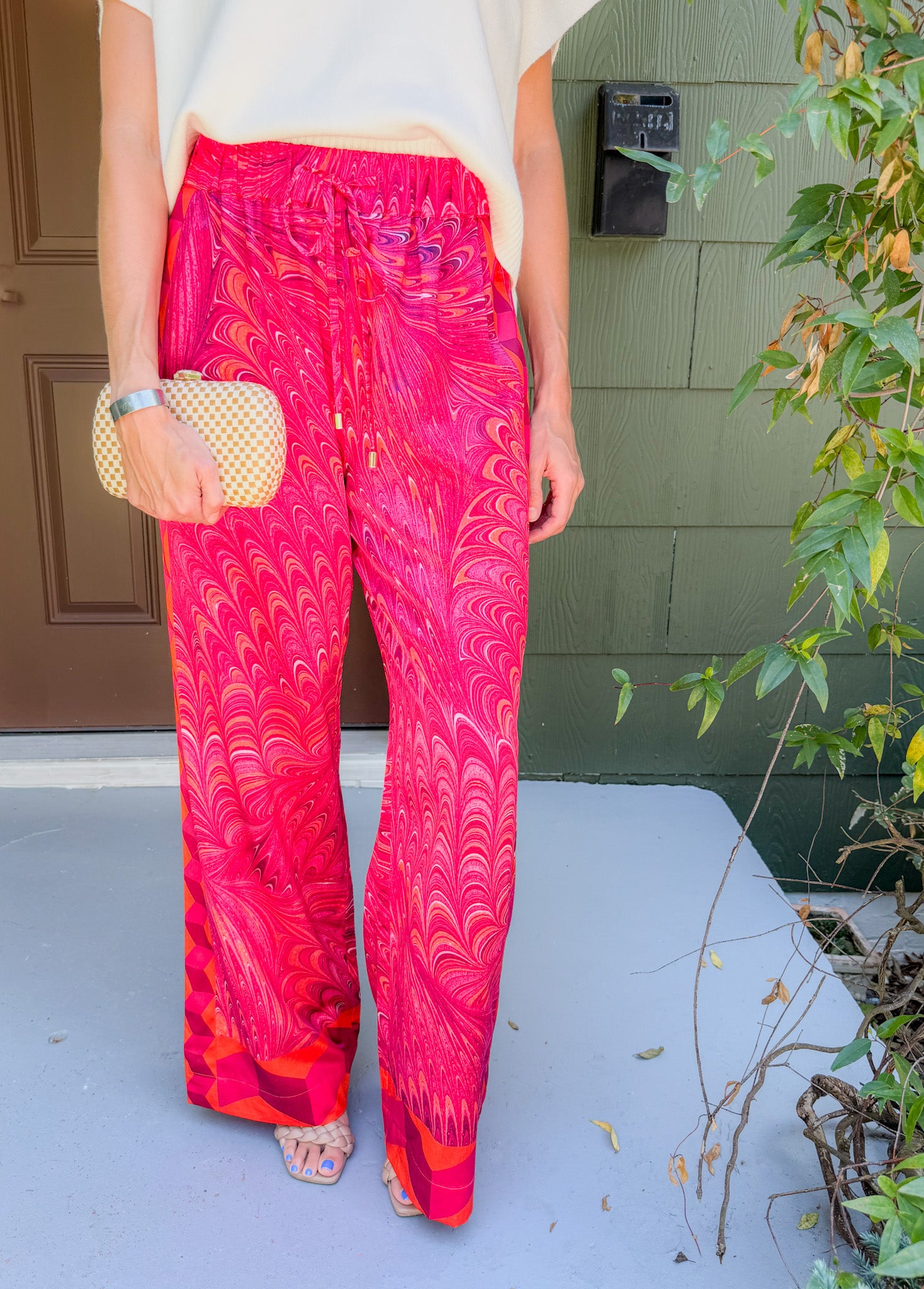 Person wearing bright pink patterned pants with a white top, standing on a porch.