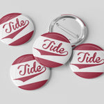 Four round pin-back buttons with a white and dark red design featuring the word 'Tide' in cursive, with one button showing the metal pin-back backing, on a light gray background.