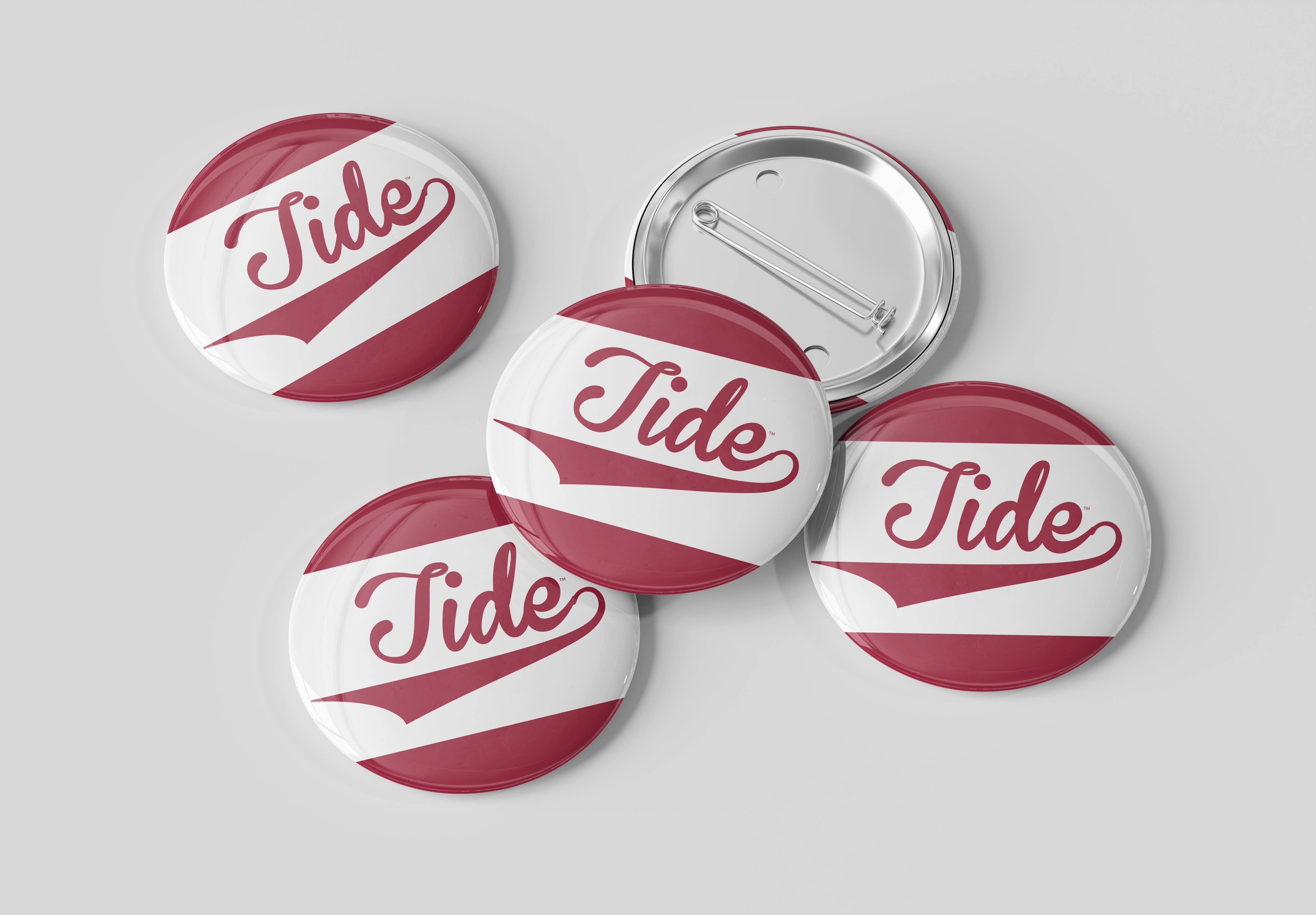 Four round pin-back buttons with a white and dark red design featuring the word 'Tide' in cursive, with one button showing the metal pin-back backing, on a light gray background.