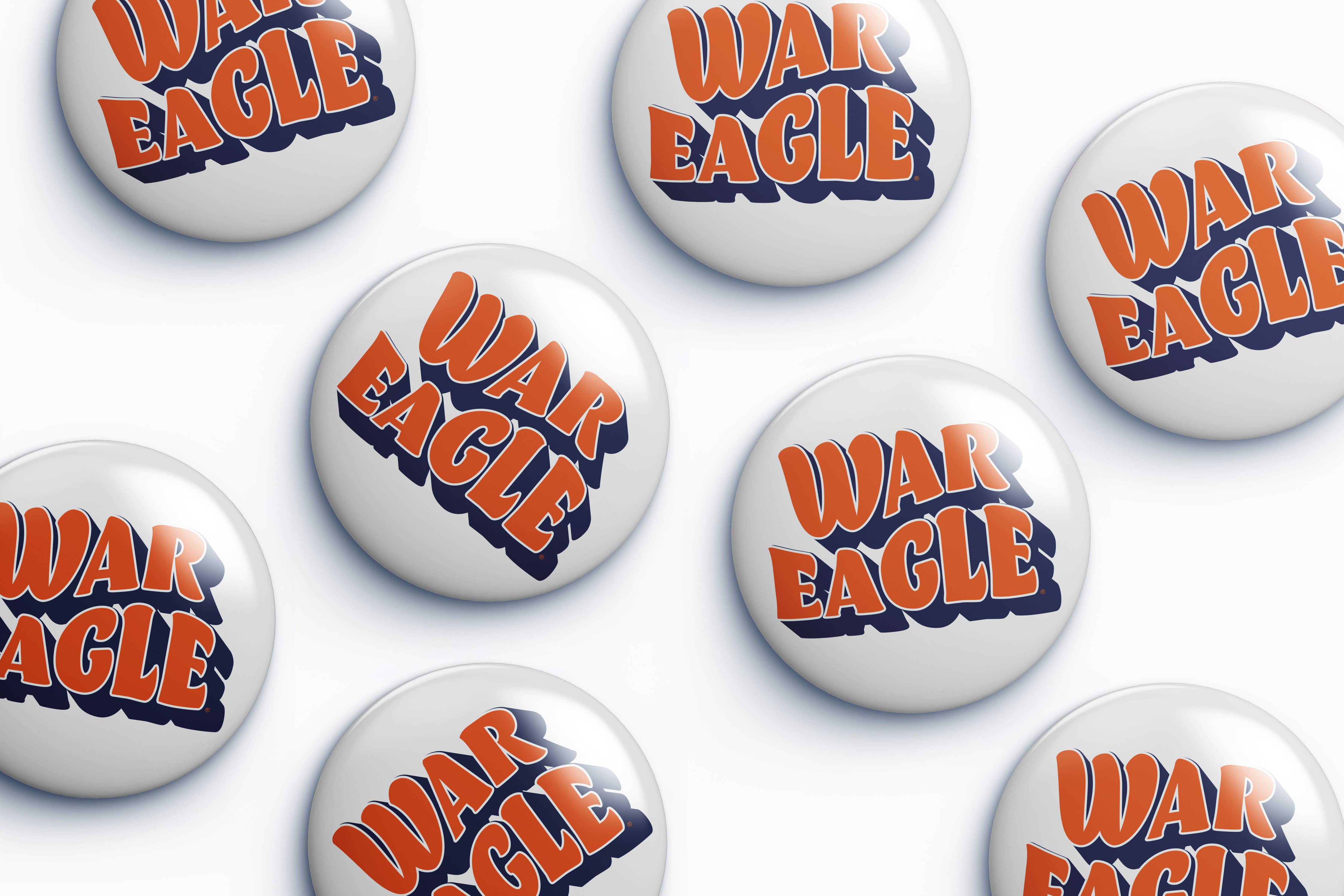 Several round white button badges with the words "WAR EAGLE" in orange and navy blue are arranged on a light gray background.