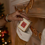 Hand placing a Votivo candle inside a decorated stocking with a warm, festive background.