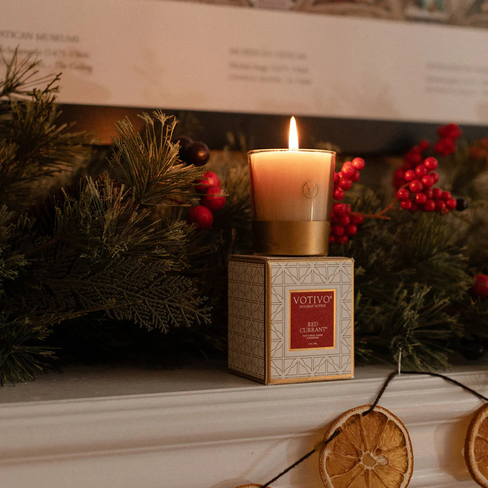 Votive candle in a decorative box on a mantelpiece with Christmas decorations.