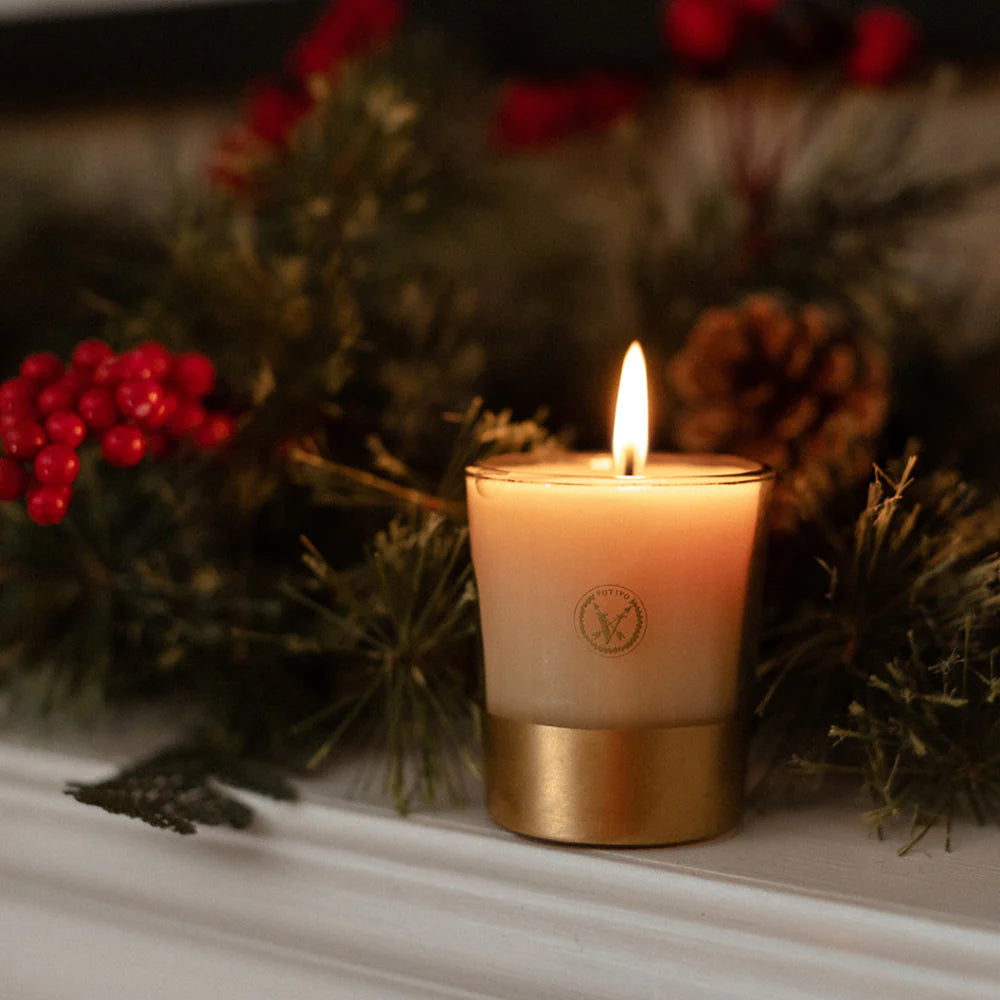 Candle with a gold base and greenery and berries in the background