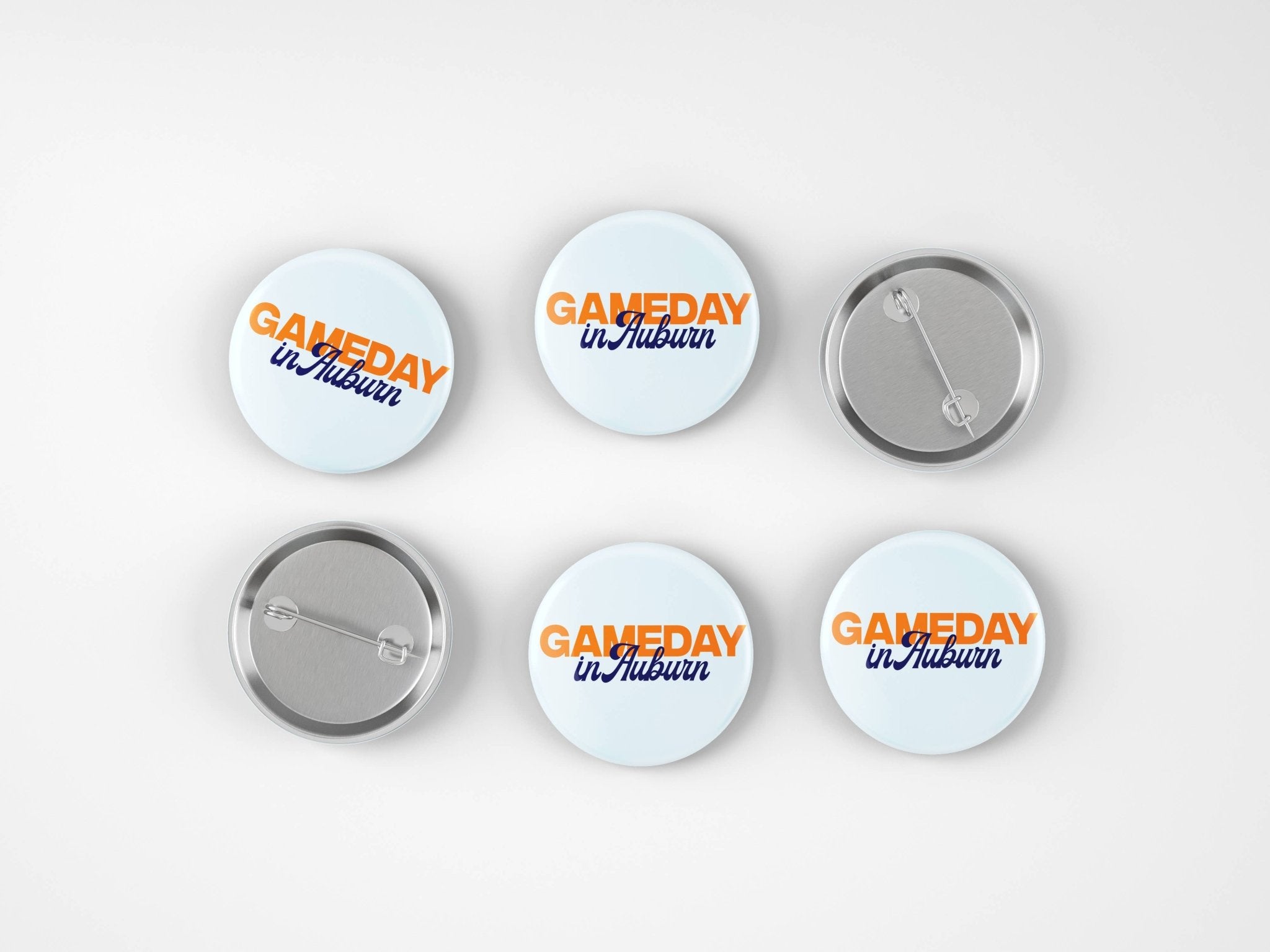 Six round pin-back buttons shown on a light gray background, including three front views and three back views. The front buttons have a white background with orange and blue text reading 'GAMEDAY in Auburn'.