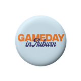 A round light blue button badge featuring the text 'GAMEDAY in Auburn' in orange and navy blue lettering, centered on a plain white background.