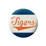 A round button badge featuring the word 'Tigers' in orange script across a white center, with dark blue bands at the top and bottom, shown on a plain white background.