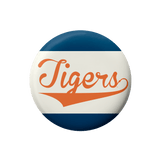 A round button badge featuring the word 'Tigers' in orange script across a white center, with dark blue bands at the top and bottom, shown on a plain white background.