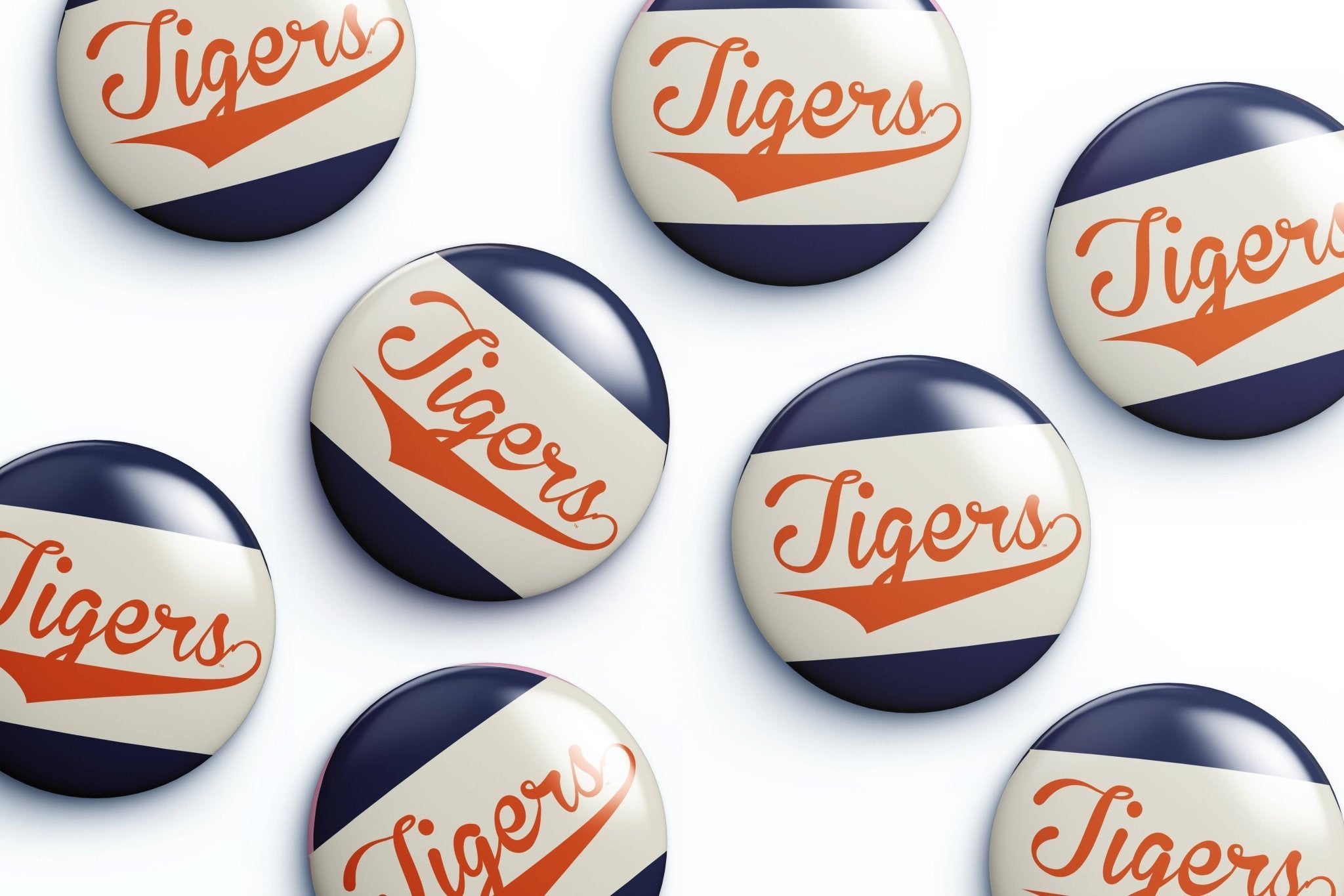 Several round glossy buttons with the word "Tigers" in orange script over diagonal navy and off-white stripes, arranged on a white background.