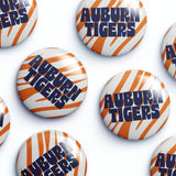 Several round button badges with the Auburn Tigers logo, featuring orange and white tiger stripes and navy blue lettering, arranged on a white background.