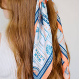 Woman with long brown hair wearing a patterned orange and blue hair scarf.