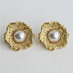 Pair of gold earrings with pearl centers on a light gray background