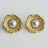 Pair of gold earrings with pearl centers on a light gray background