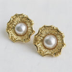 Pair of gold earrings with pearl centers on a light gray background