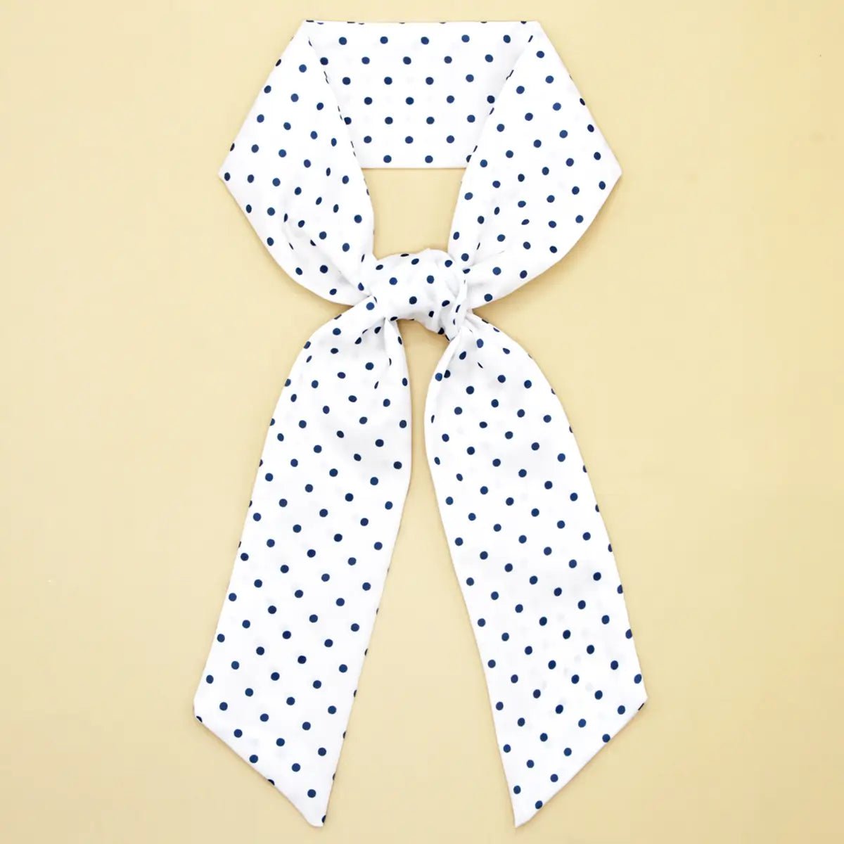 White scarf with navy blue polka dots on a beige background